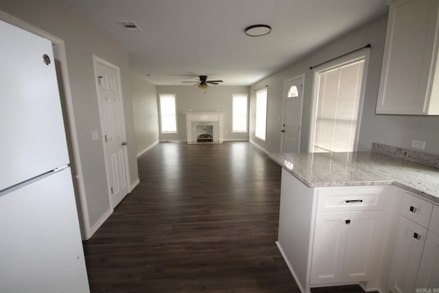 kitchen featuring visible vents, a fireplace, ceiling fan, dark wood-type flooring, and white cabinetry