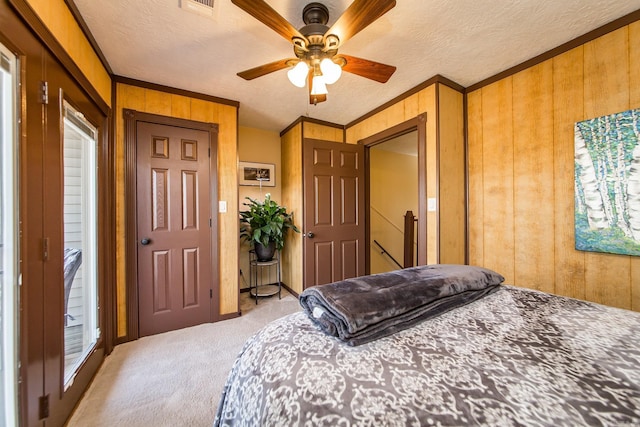 bedroom with wooden walls, crown molding, ceiling fan, light colored carpet, and a textured ceiling