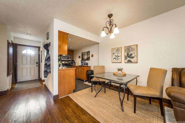 dining area featuring dark wood finished floors, a notable chandelier, a textured ceiling, and baseboards