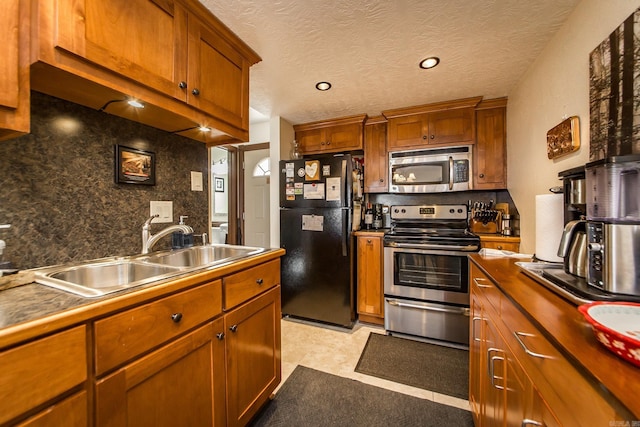 kitchen featuring a sink, backsplash, appliances with stainless steel finishes, and brown cabinetry