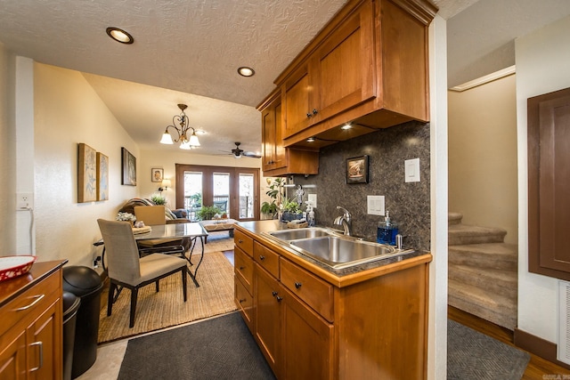 kitchen featuring brown cabinets, a sink, a textured ceiling, tasteful backsplash, and open floor plan