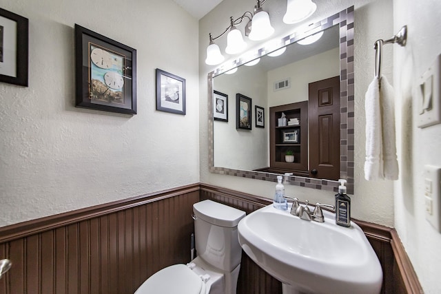 half bathroom featuring visible vents, toilet, a sink, wood walls, and wainscoting