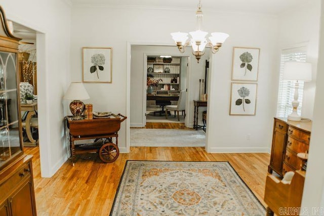 interior space featuring an inviting chandelier, light wood-style floors, baseboards, and ornamental molding