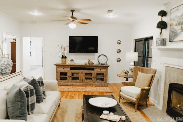 living room featuring wood finished floors, visible vents, a fireplace, ornamental molding, and ceiling fan