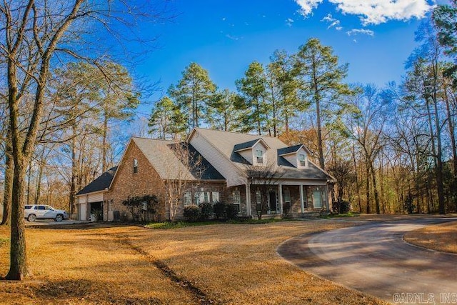 cape cod home featuring an attached garage, driveway, and a front lawn