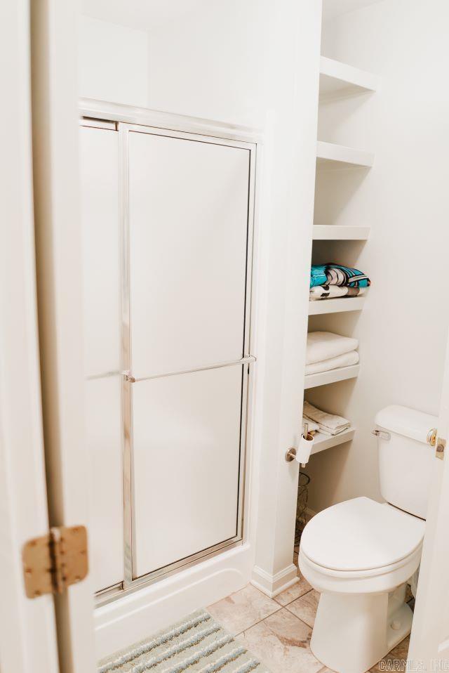 bathroom featuring toilet, a stall shower, and tile patterned flooring