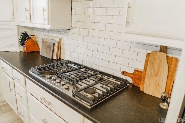 kitchen featuring decorative backsplash, dark countertops, white cabinets, and stainless steel gas cooktop