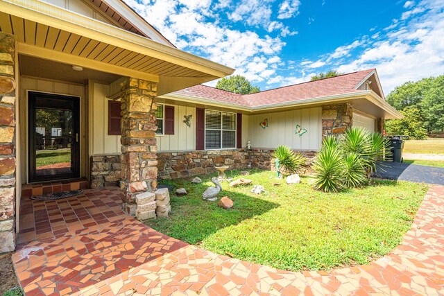 entrance to property with stone siding, board and batten siding, an attached garage, and driveway