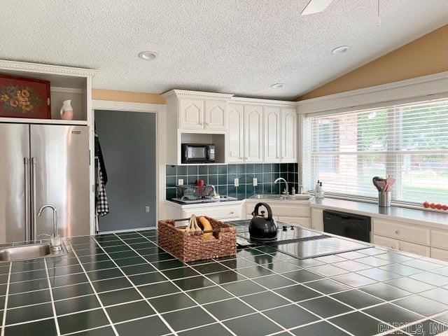 kitchen featuring black appliances, a sink, tile countertops, white cabinets, and lofted ceiling