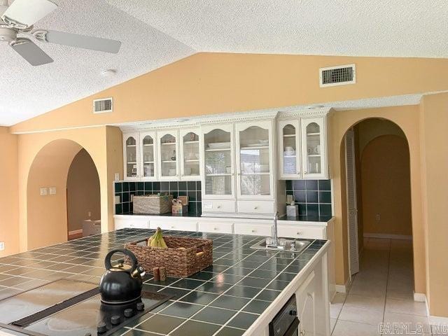 kitchen with arched walkways, visible vents, lofted ceiling, and tile counters