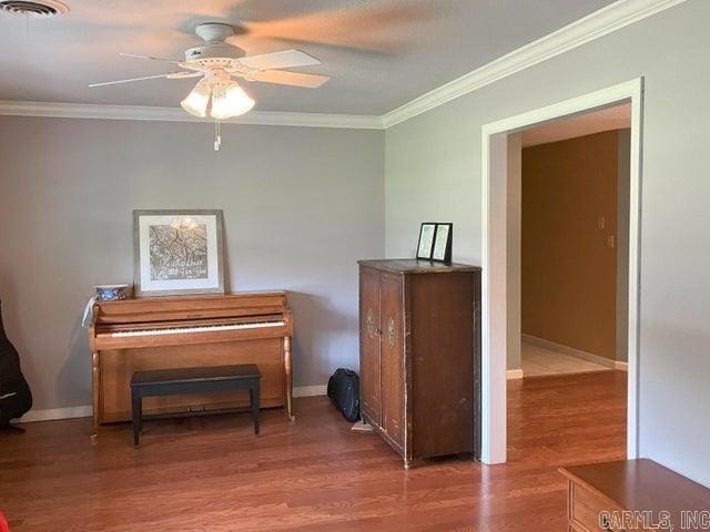 living area with baseboards, wood finished floors, a ceiling fan, and crown molding