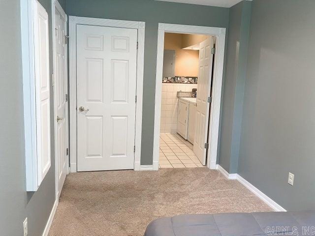 hallway featuring washing machine and dryer, light colored carpet, and baseboards