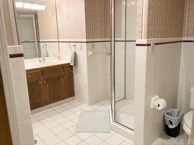 bathroom featuring a wainscoted wall, wallpapered walls, a shower stall, tile walls, and tile patterned floors