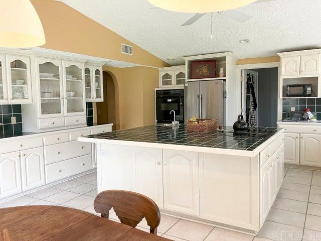 kitchen featuring glass insert cabinets, tile counters, a center island with sink, lofted ceiling, and black appliances