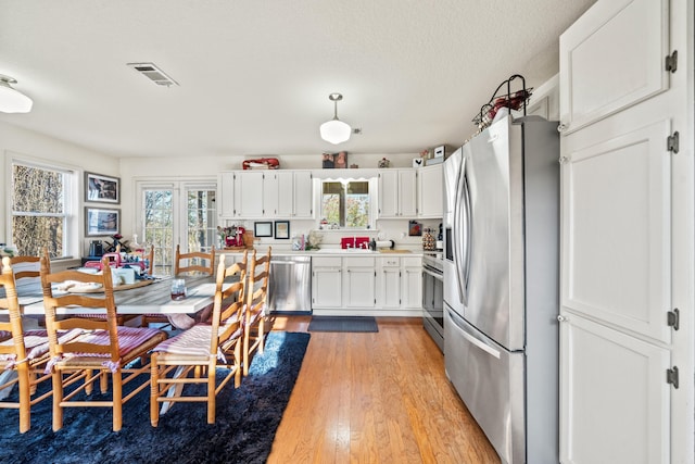 kitchen with visible vents, white cabinets, stainless steel appliances, and light wood-type flooring