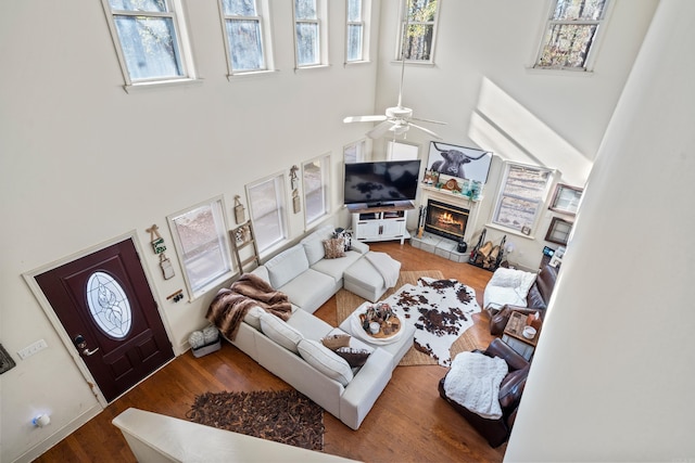 living area with a towering ceiling, wood finished floors, a glass covered fireplace, and a ceiling fan