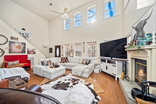 living room featuring wood finished floors, a ceiling fan, visible vents, plenty of natural light, and a glass covered fireplace