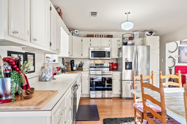 kitchen featuring light wood finished floors, visible vents, appliances with stainless steel finishes, white cabinetry, and a sink