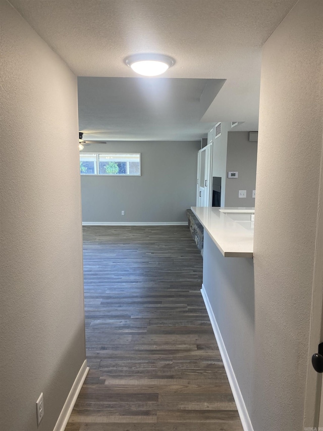 corridor with baseboards, a textured ceiling, and dark wood-style flooring