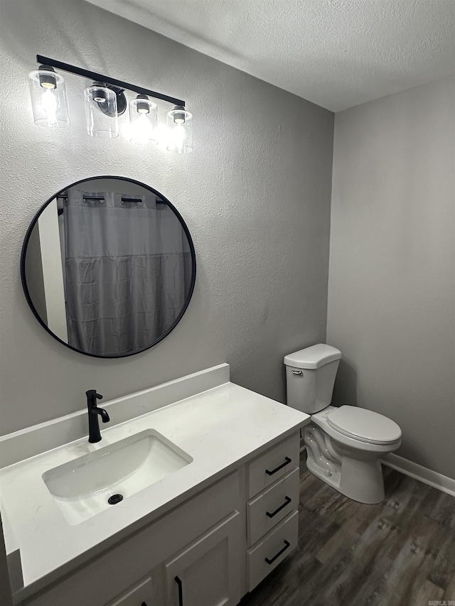 bathroom with vanity, wood finished floors, a textured ceiling, toilet, and a textured wall