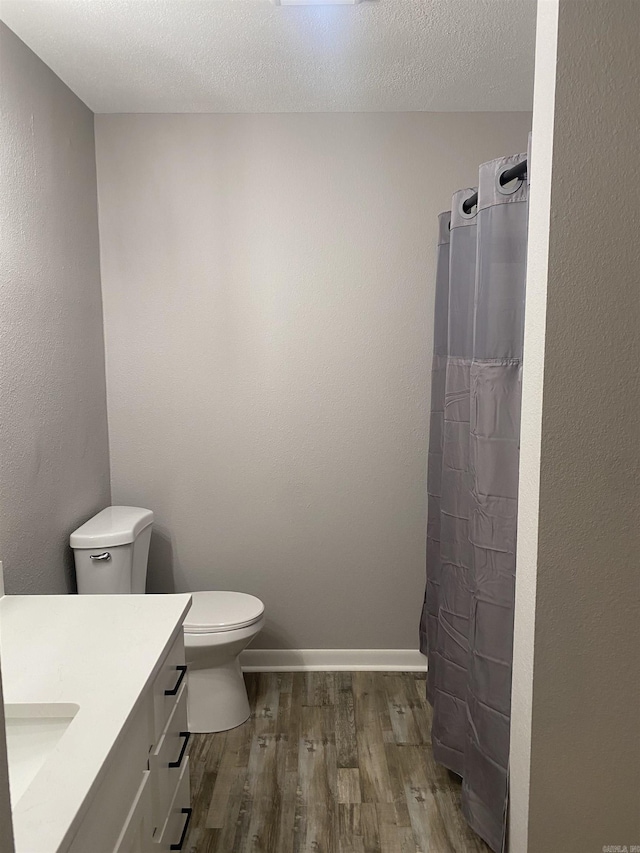 full bath with toilet, a textured ceiling, wood finished floors, baseboards, and vanity