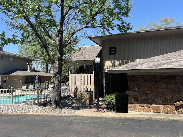 view of front of home featuring an outdoor pool, stone siding, roof with shingles, and fence