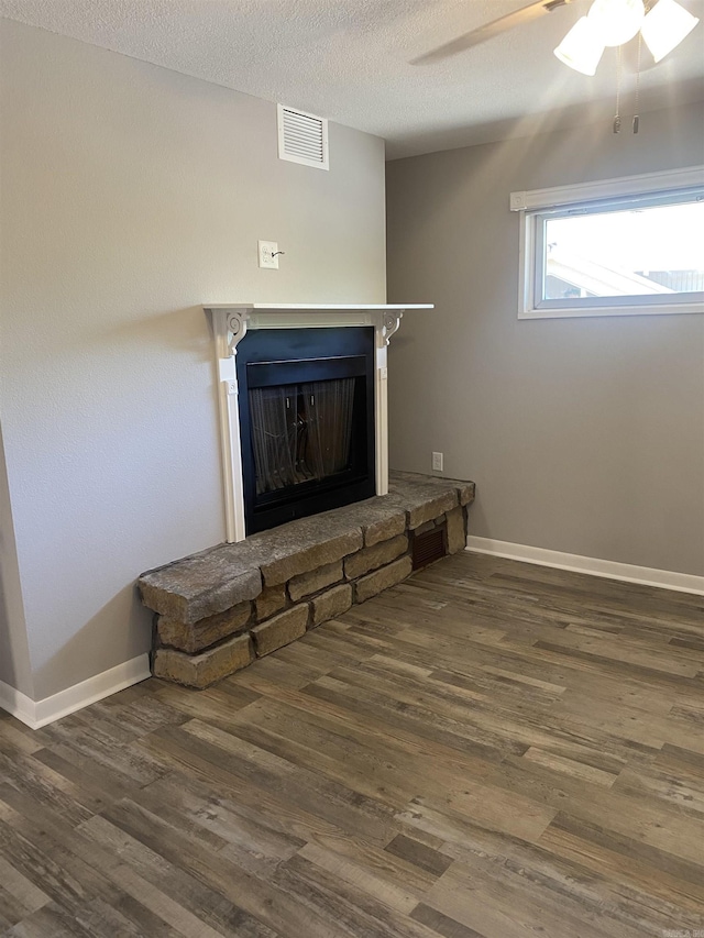 room details with wood finished floors, visible vents, a fireplace with raised hearth, ceiling fan, and a textured ceiling