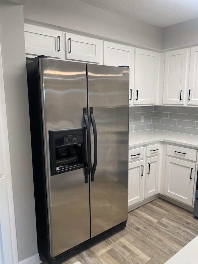 kitchen featuring light countertops, light wood-style flooring, stainless steel refrigerator with ice dispenser, and white cabinets