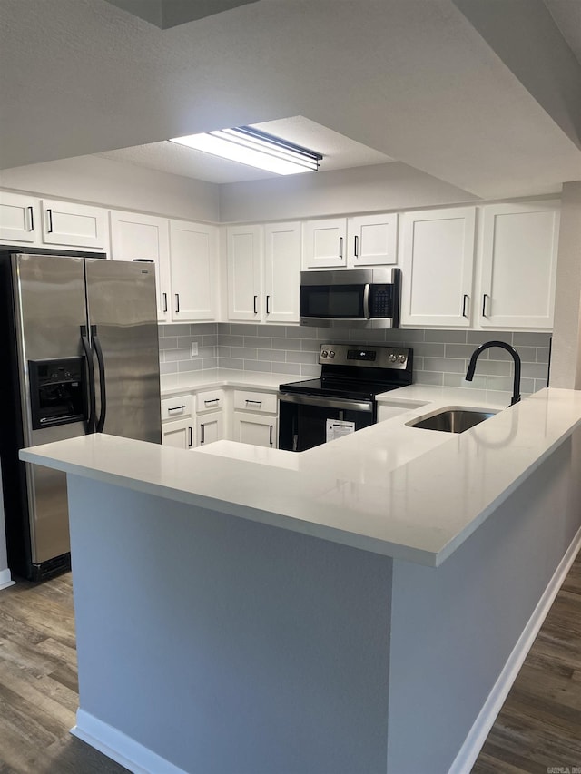 kitchen featuring dark wood finished floors, a peninsula, stainless steel appliances, and a sink