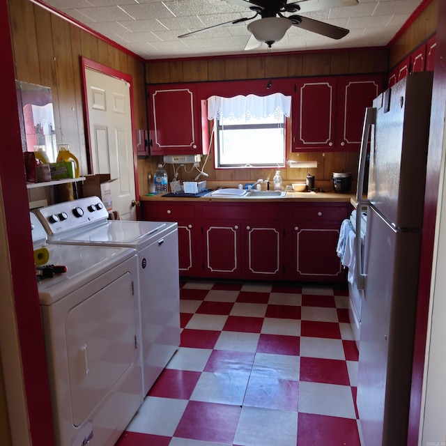 kitchen with wooden walls, a ceiling fan, dark floors, freestanding refrigerator, and washing machine and dryer