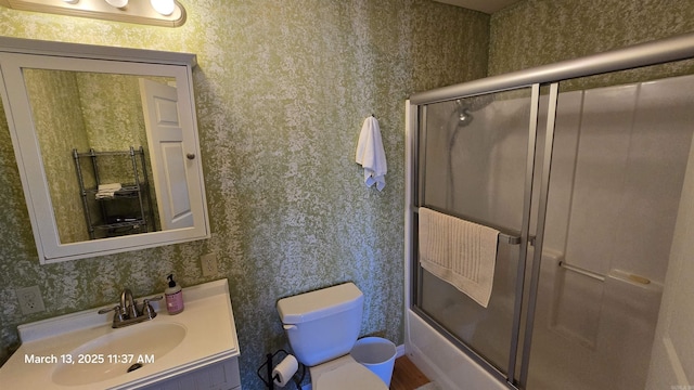 bathroom with bath / shower combo with glass door, toilet, vanity, and wallpapered walls