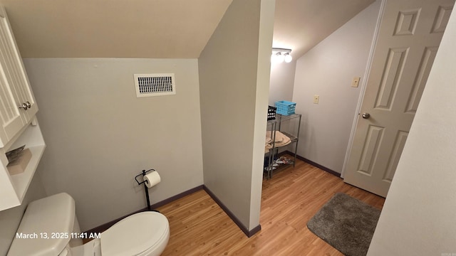 half bathroom with visible vents, baseboards, toilet, vaulted ceiling, and wood finished floors