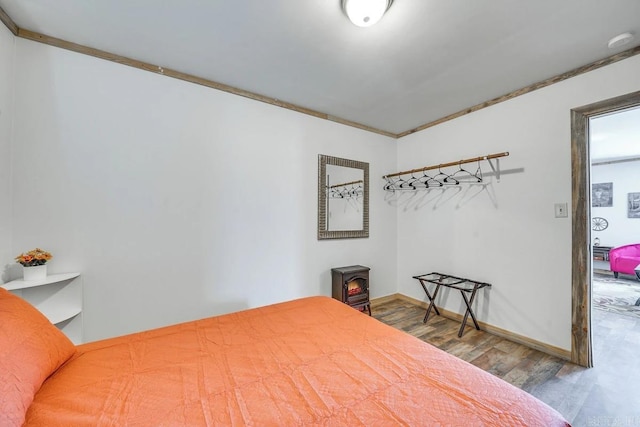 bedroom featuring ornamental molding, baseboards, wood finished floors, and a wood stove