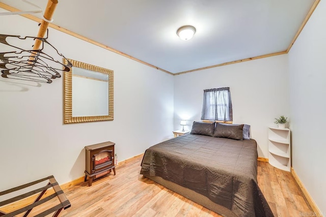 bedroom with wood finished floors, a wood stove, crown molding, and baseboards