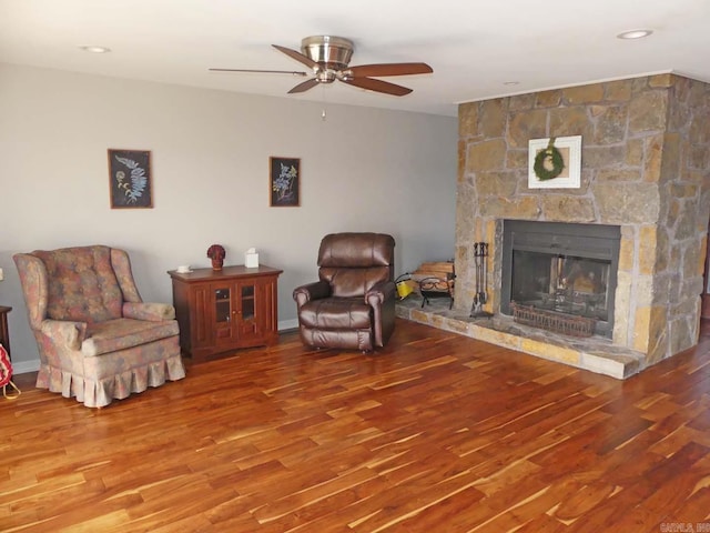 sitting room with a stone fireplace, a ceiling fan, and wood finished floors