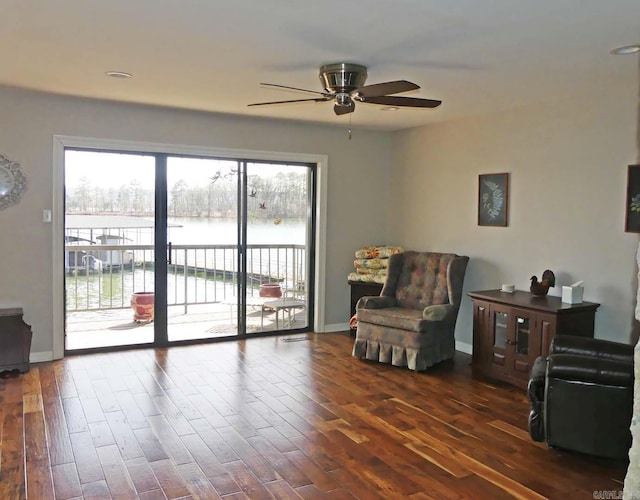 living area with dark wood-type flooring, a ceiling fan, and a water view