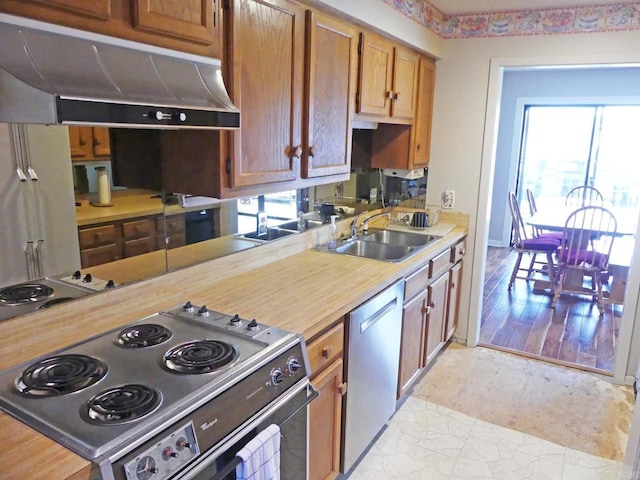 kitchen featuring under cabinet range hood, light countertops, appliances with stainless steel finishes, brown cabinetry, and a sink