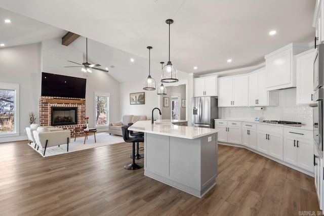 kitchen with backsplash, open floor plan, beam ceiling, appliances with stainless steel finishes, and a ceiling fan