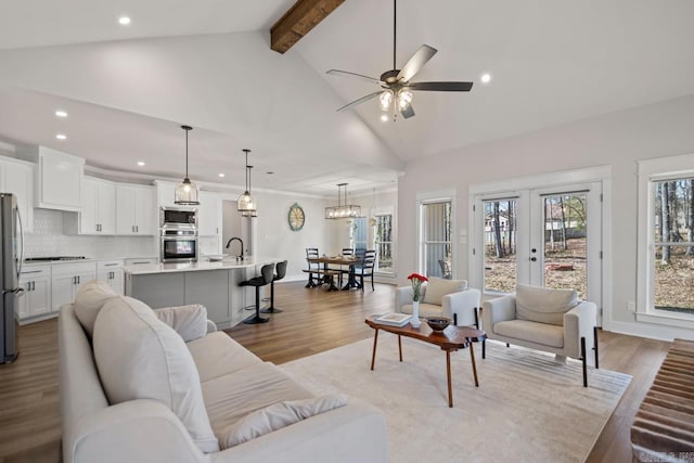 living room featuring light wood-type flooring, beam ceiling, high vaulted ceiling, and ceiling fan