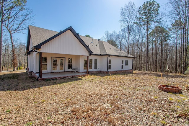 rear view of house with a shingled roof, a patio, french doors, and a fire pit