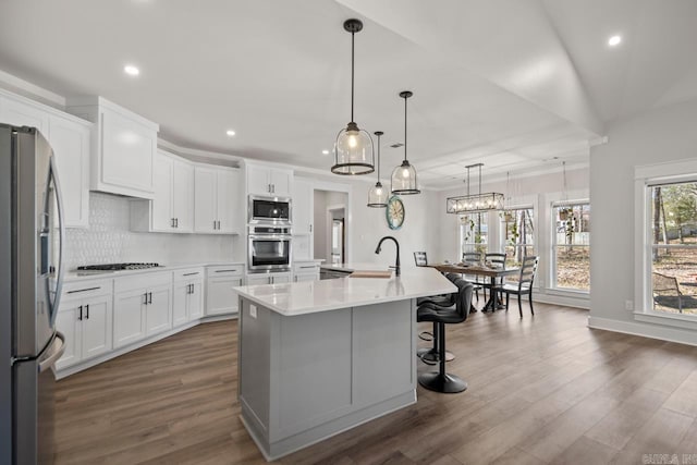 kitchen with a kitchen island with sink, backsplash, appliances with stainless steel finishes, light countertops, and dark wood-style flooring