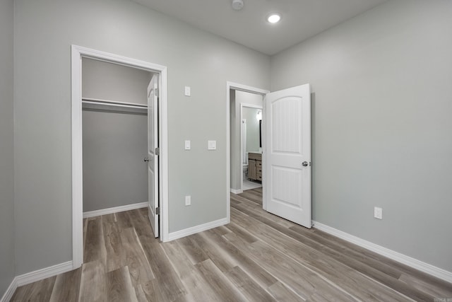 unfurnished bedroom with a walk in closet, wood finished floors, baseboards, and a closet