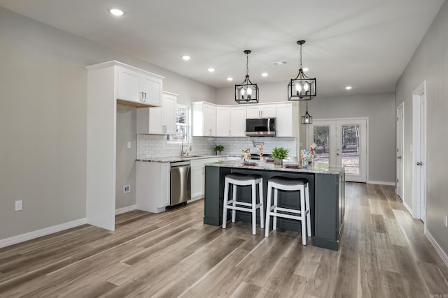 kitchen featuring light wood-type flooring, backsplash, a center island, stainless steel appliances, and white cabinets