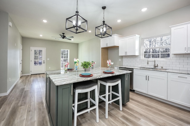 kitchen with a sink, tasteful backsplash, white cabinets, and ceiling fan with notable chandelier