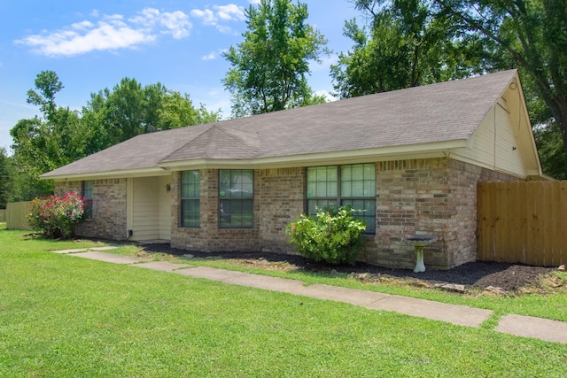 ranch-style house with a front yard, fence, brick siding, and roof with shingles