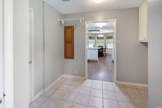 hall with a notable chandelier, light tile patterned floors, baseboards, and a textured ceiling