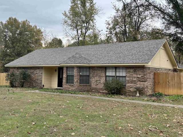 ranch-style home with a front yard, fence, brick siding, and roof with shingles