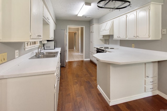 kitchen with premium range hood, a sink, a textured ceiling, dark wood finished floors, and a peninsula