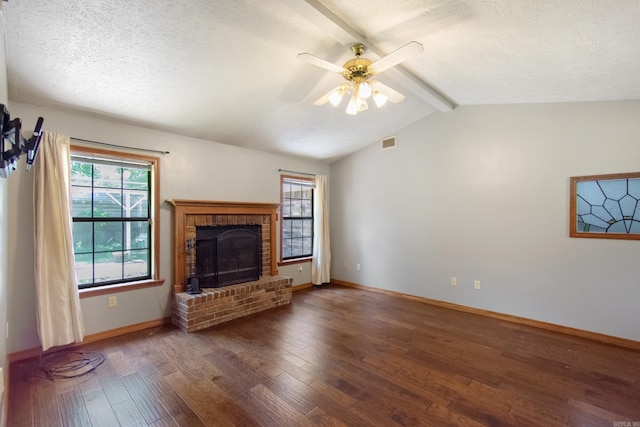 unfurnished living room with a brick fireplace, vaulted ceiling with beams, ceiling fan, wood finished floors, and a textured ceiling