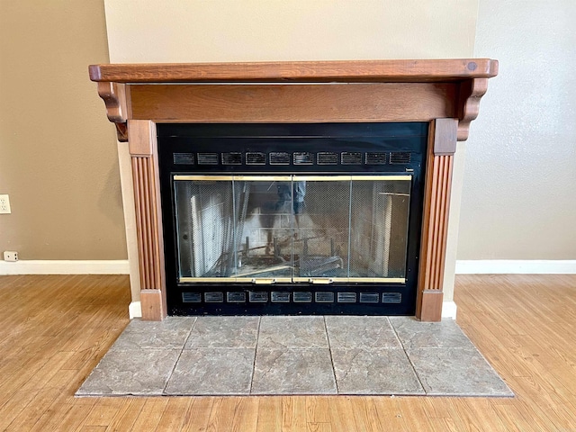 details with a glass covered fireplace, wood finished floors, and baseboards